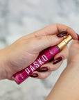 Hand holding a pink Pasko Perfume Bottle with against a blurred background