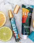 Pasko Valencia hand cream and spray bottle with citrus fruits on a marble surface