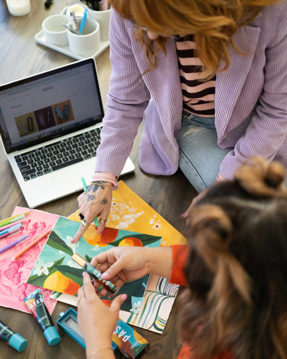 Two people working on a creating Pasko with colorful materials and a laptop in the background.