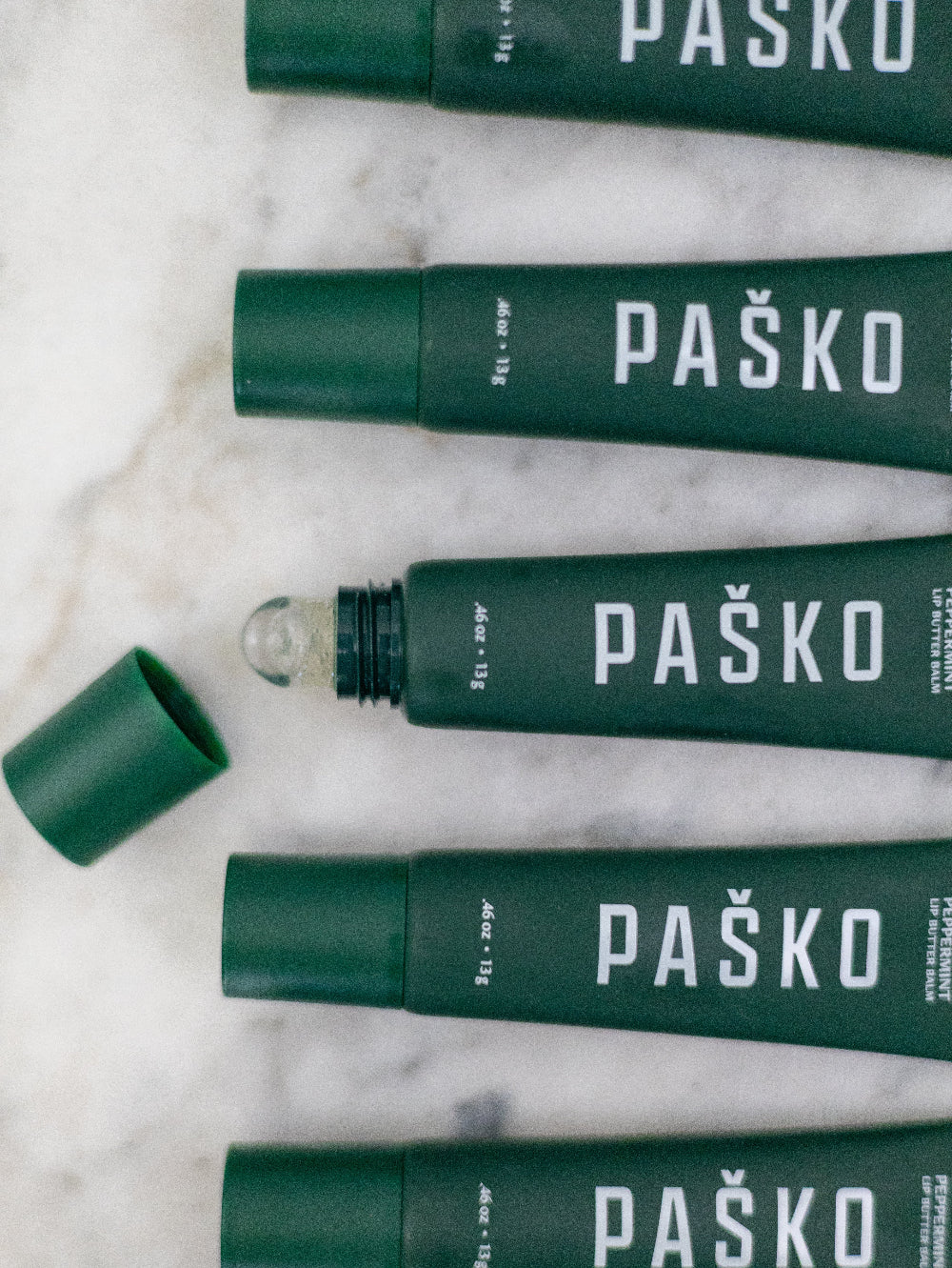 Green Mint Pasko lip balm tubes on a marble surface