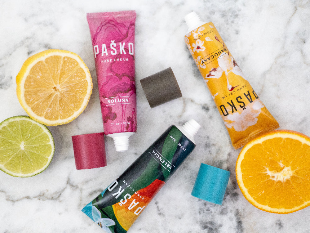 Colorful Pasko hand cream tubes on a marble surface with citrus fruits.