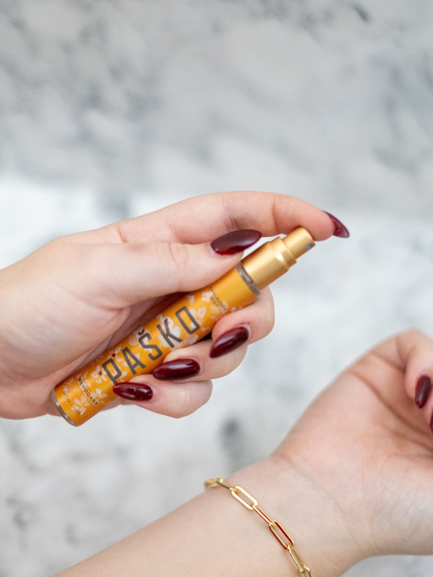 Hand holding a yellow Pasko perfume against a marble background