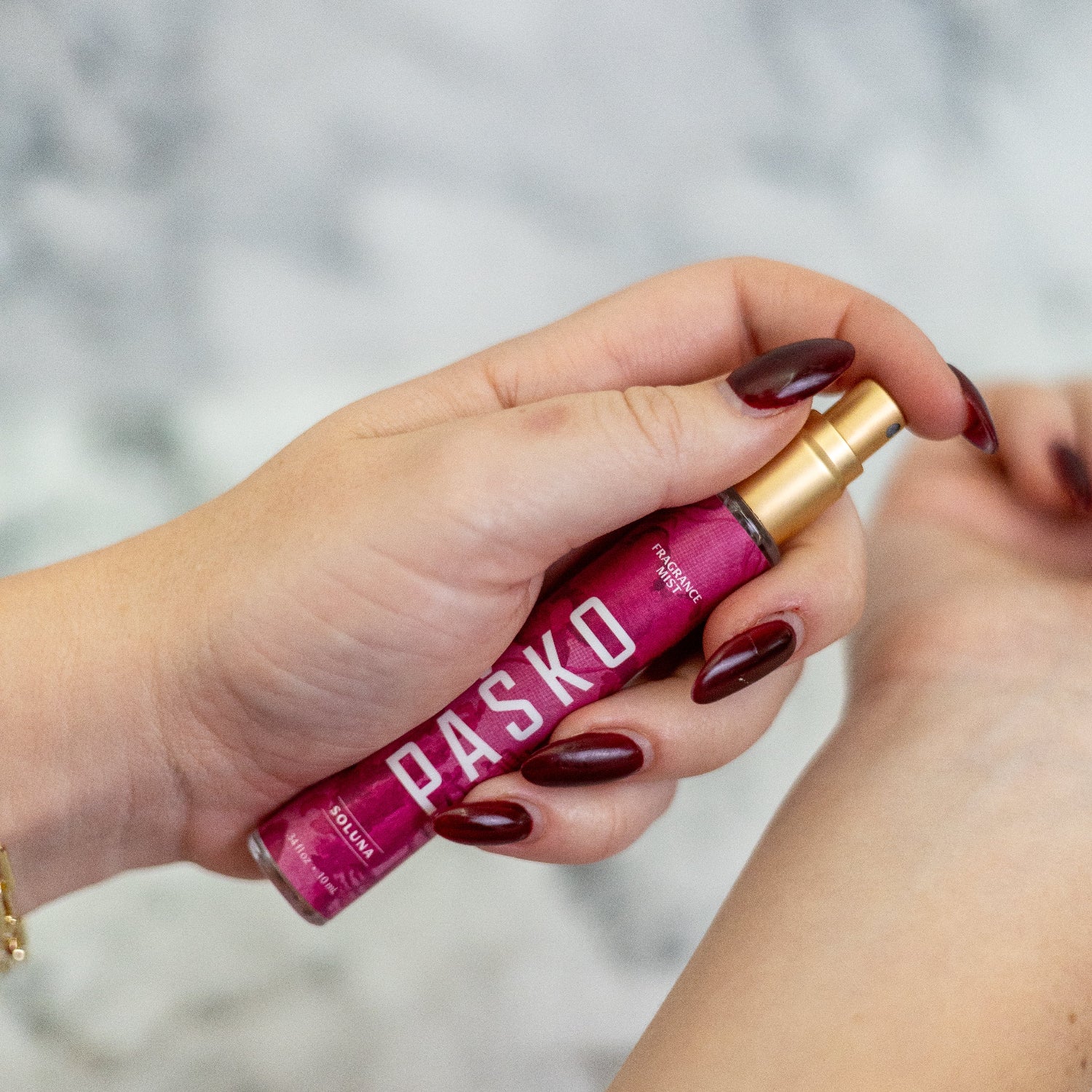 Hand holding a pink Pasko Perfume Bottle with  against a blurred background