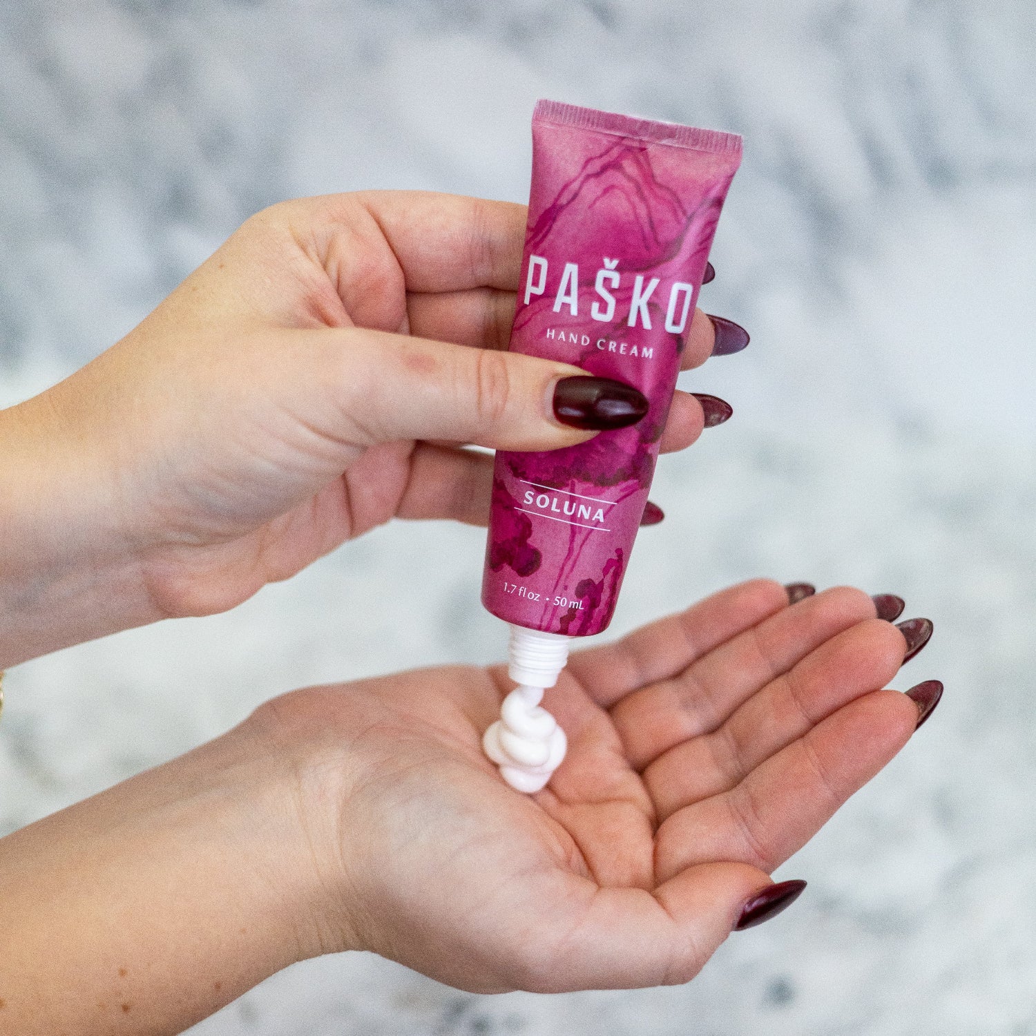 Hand holding a pink tube of Pasko Soluna hand cream with a blurred background
