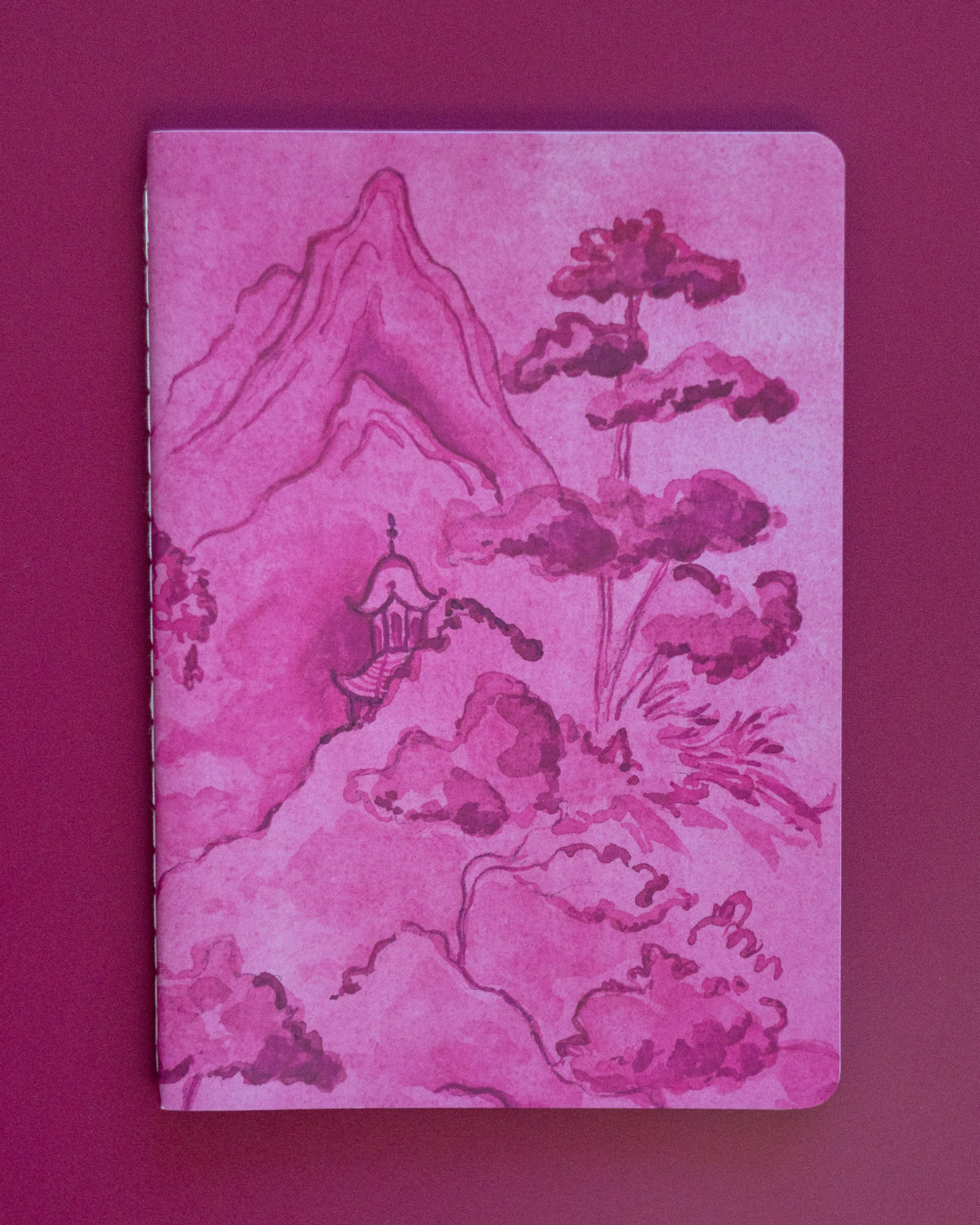 Pink notebook with mountain and cloud design on a pink background