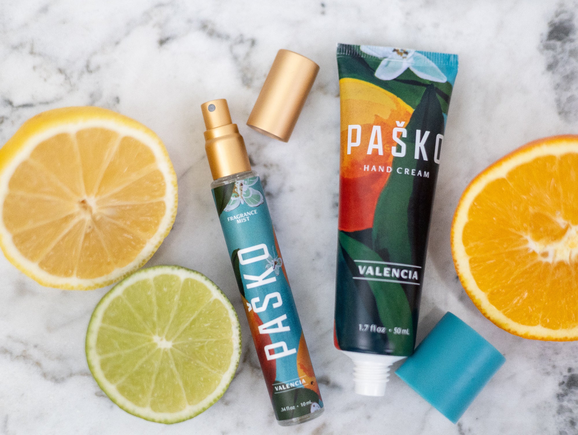 Pasko Valencia hand cream and spray bottle with citrus fruits on a marble surface