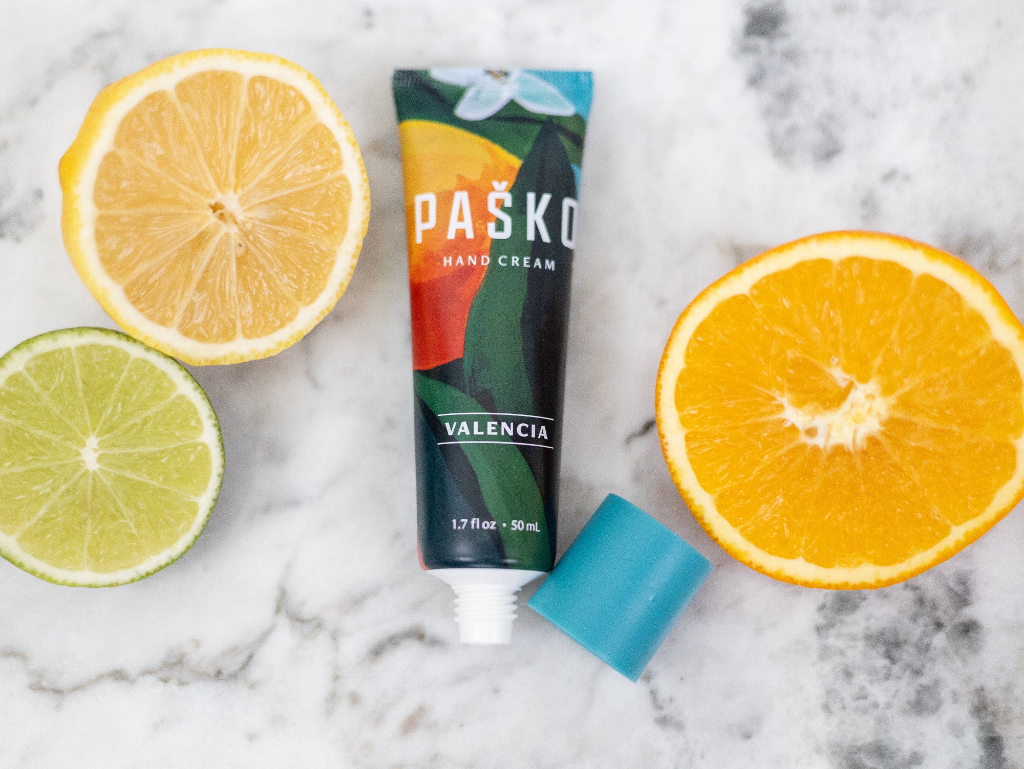 Pasko Valencia hand cream tube with sliced lemon, lime, and orange on a marble background